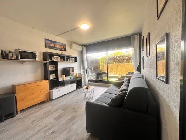 Een moderne woonkamer met een grijze bank, een televisie en een houten kast.