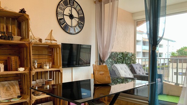 Una sala de estar con una estantería de madera, una mesa con superficie de vidrio, un reloj negro y un televisor.
