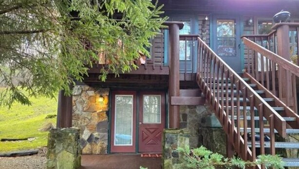 Un chalet rustique avec une façade en pierre, un revêtement extérieur en bois et un escalier en bois menant à une terrasse.