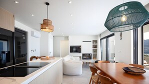 Une cuisine moderne dotée d’un îlot central, d’une table à manger en bois et d’une grande fenêtre offrant une vue dégagée.