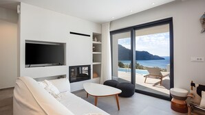 Un salon moderne avec un canapé blanc, un téléviseur à écran plat et une vue sur la mer grâce à de grandes portes vitrées.
