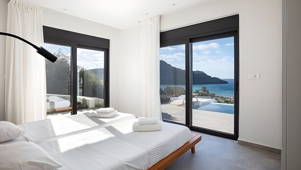 Une chambre moderne avec un grand lit, deux fenêtres et une vue sur la mer.