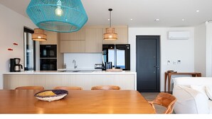 Une cuisine moderne dotée d’un îlot central, de luminaires suspendus et d’un coin repas avec une table et des chaises en bois.