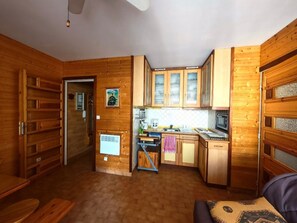 A compact kitchen with wooden cabinets, a microwave, and a small dining area. - Canet-en-Roussillon T2 Beachfront with Parking - Perfect for 4 (Canet-en-Roussillon)