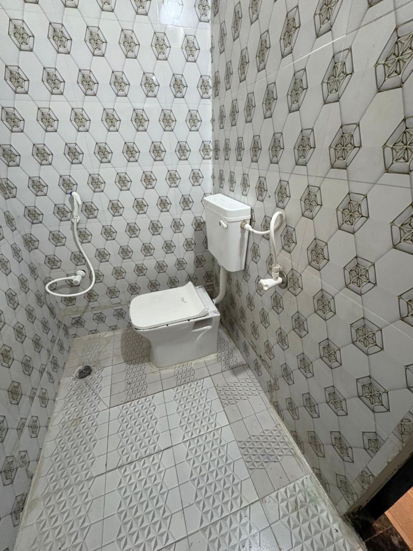 Een badkamer met tegels in een honingraatpatroon, een toilet en een douchehoek.