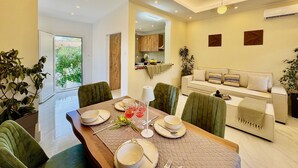 Uma sala de jantar moderna com uma mesa de madeira posta para quatro, um sofá e uma cozinha ao fundo.