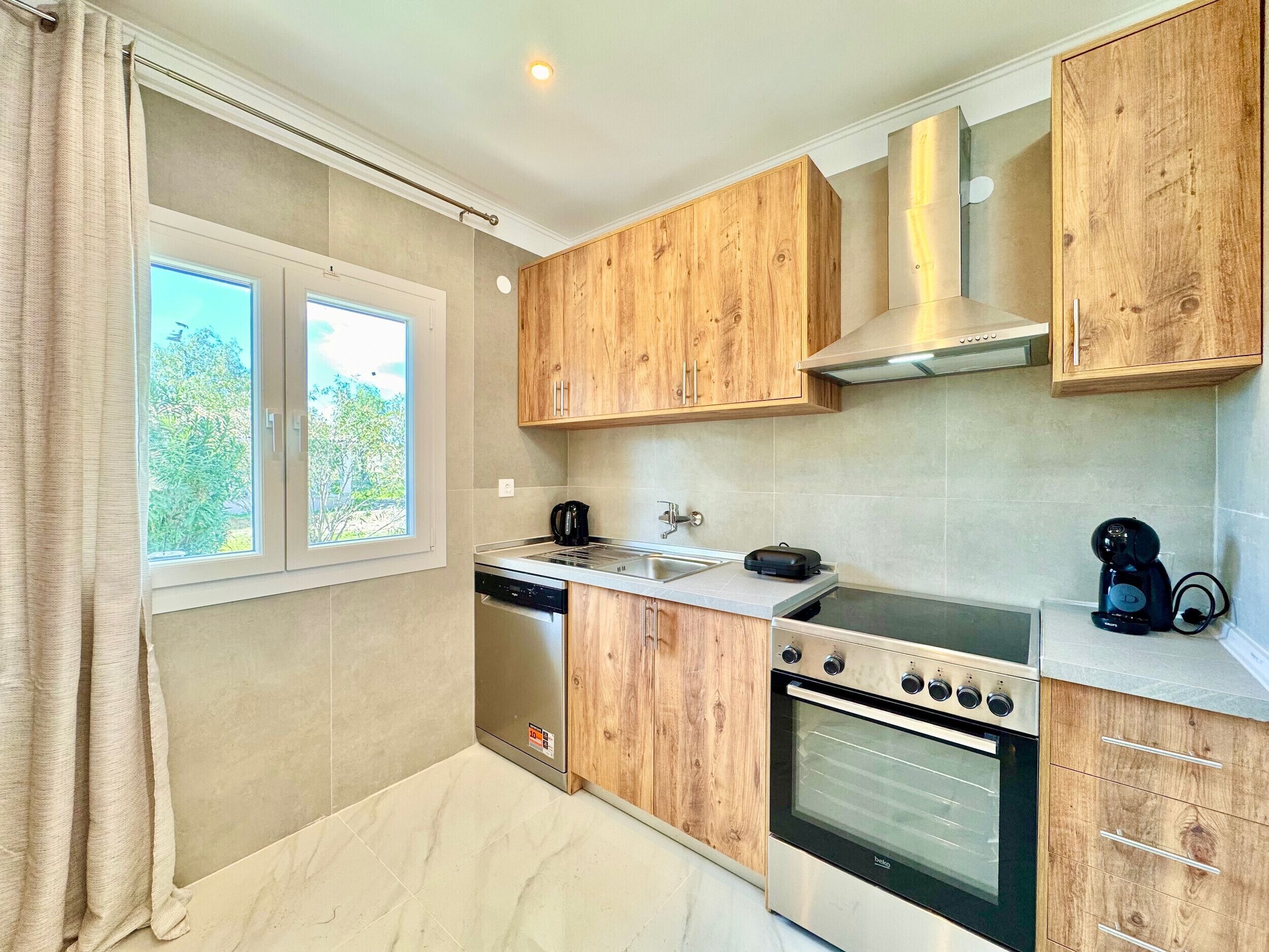 A compact kitchen with wooden cabinets, a built-in oven, and a window with a view of greenery.