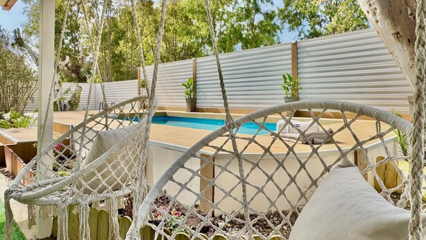 Uma cadeira rede, uma piscina e um deck de madeira.