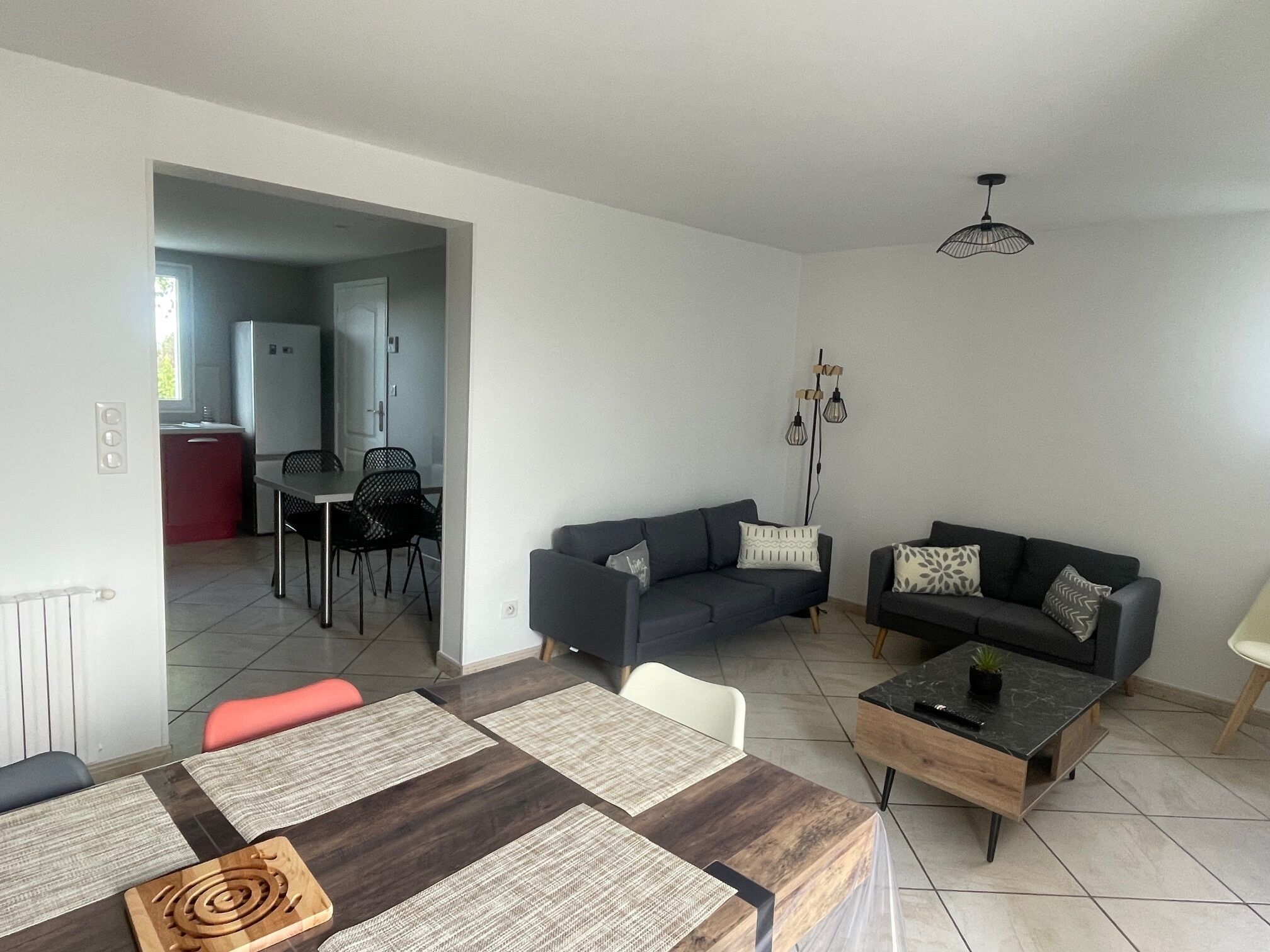 Ein modernes Wohnzimmer mit Essbereich, zwei Sofas, einem Couchtisch und einer durch einen offenen Durchgang sichtbaren Küche.