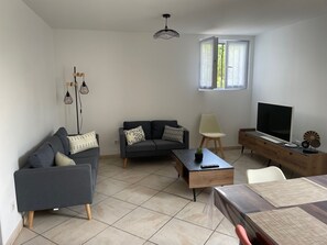 Ein modernes Wohnzimmer mit Sofa, Couchtisch, Fernseher und einem Essbereich mit Tisch und Stühlen.