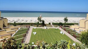 Blick auf den Strand vom Hotelbalkon mit Pool und Liegestühlen.