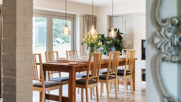 A dining area with a wooden table and chairs, hanging pendant lights, and a vase with flowers. - Luxury Countryside Retreat with Pool | Surrey Hills Escape - Pass the Keys (Leatherhead)