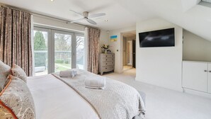 A bedroom with a large bed, a ceiling fan, a TV mounted on the wall, and a sliding glass door leading to a balcony. - Luxury Countryside Retreat with Pool | Surrey Hills Escape - Pass the Keys (Leatherhead)