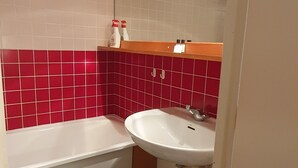Et badeværelse med et hvidt badekar, et hvidt håndvask og røde fliser på væggene.