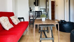 En moderne stue med en rød sofa, et spisebord med stole, et køkken i baggrunden og en sort læderpude.