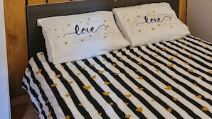 Una cama con una colcha a rayas negras y blancas y dos almohadas con la palabra 'love' y pequeños corazones.