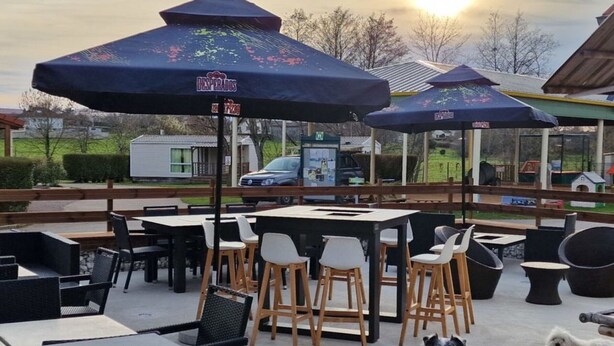 An outdoor patio area with tables and chairs, umbrellas, and a dog. - Cosy Mobile Home 6 Pers with Terrace (Radonvilliers)