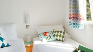 A bedroom with two beds, a nightstand, a window with a curtain, and a green box on the floor. - Cosy Mobile Home 6 Pers with Terrace (Radonvilliers)