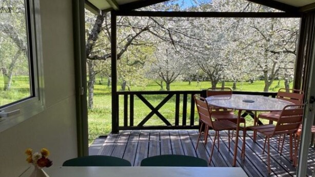 A covered outdoor area with a table and chairs, a view of a garden with trees, and a wooden deck. - Comfortable 2-Bedroom Chalet with Terrace in Vébron (Vebron)