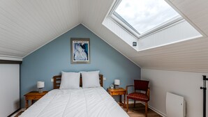 A bedroom with a sloped ceiling, a skylight, a bed with white bedding, two bedside tables with lamps, a chair, and a radiator. - 3-Bed House 100m from Beach (Biscarrosse)