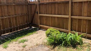 A wooden fence, a small garden with green plants, and a building with a tiled roof in the background. - 3-Bed House 100m from Beach (Biscarrosse)