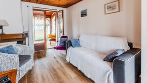 A cozy room with a wooden ceiling, a white sofa, a wicker chair, and a small table with a lamp. - 3-Bed House 100m from Beach (Biscarrosse)