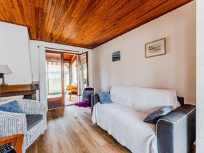 A cozy room with a wooden ceiling, a white sofa, a wicker chair, and a small table with a lamp. - 3-Bed House 100m from Beach (Biscarrosse)