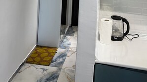 Un couloir étroit doté d’un sol à motifs de marbre, d’un réfrigérateur blanc et d’un coin cuisine comprenant une bouilloire et un rouleau d’essuie-tout.