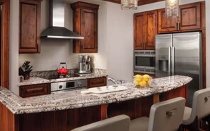 Cozinha com armários de madeira, bancadas de granito, eletrodomésticos de aço inoxidável e um bar embutido com banquetas.