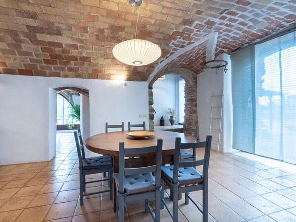A dining area with a brick ceiling, a round wooden table, and six upholstered chairs.