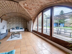 A spacious living area with a curved brick ceiling, a white sofa with blue cushions, a glass coffee table, and a view of an outdoor patio.