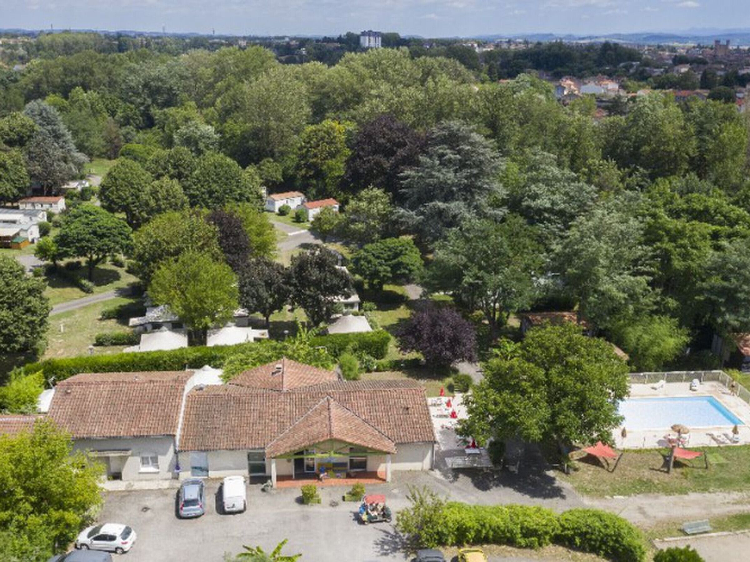 A residential area with a house featuring a tiled roof, a swimming pool, and a parking area.