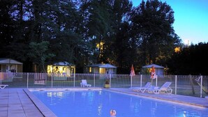 En swimmingpool med liggestole og parasoller, omgivet af et hegn og træer.
