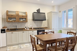 A kitchen with a dining table and chairs, a built-in stove, and a TV mounted above the stove. - SE199 - Senigallia, cozy and spacious two-bedroom apartment near the city center (Senigallia)