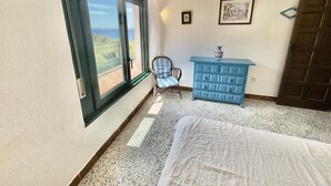 Una camera da letto con un letto, una sedia, una cassettiera e un balcone con vista.