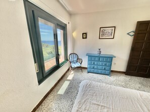 Ein Schlafzimmer mit Bett, Stuhl, Kommode und einem Balkon mit Blick.