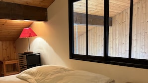 A bedroom with a bed, a nightstand, a lamp, and a window with wooden paneling.