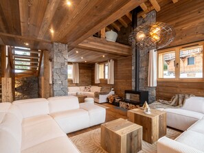 A cozy log cabin interior with a stone fireplace, wooden beams, and a large window overlooking the outside. - Luxury Chalet in Les Gets with Jacuzzi and Sauna, Pet-Friendly (Les Gets)