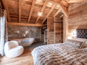 Ein Holzhütten-Interieur mit einem großen Bett, einem weißen Stuhl, einer Badewanne und einer Steinwand.
