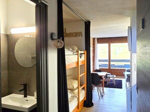 A compact room with a bed, a small desk, a chair, a round mirror, and a window. - Studio 4 pers, WIFI, Pets & Parking -- Les Gets (Les Gets)