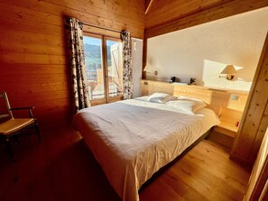 Ein Zimmer mit Holzboden, einem Bett, einem Stuhl und einem Fenster mit Vorhängen.