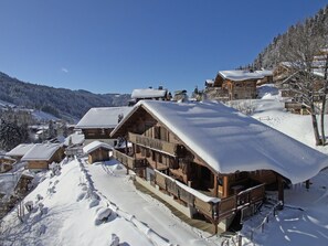 A wooden chalet-style building with a balcony, surrounded by snow-covered trees and a mountainous backdrop. - Family Chalet Les Gets - 5 beds, 4 baths, WIFI, Pets allowed, Parking (Les Gets)