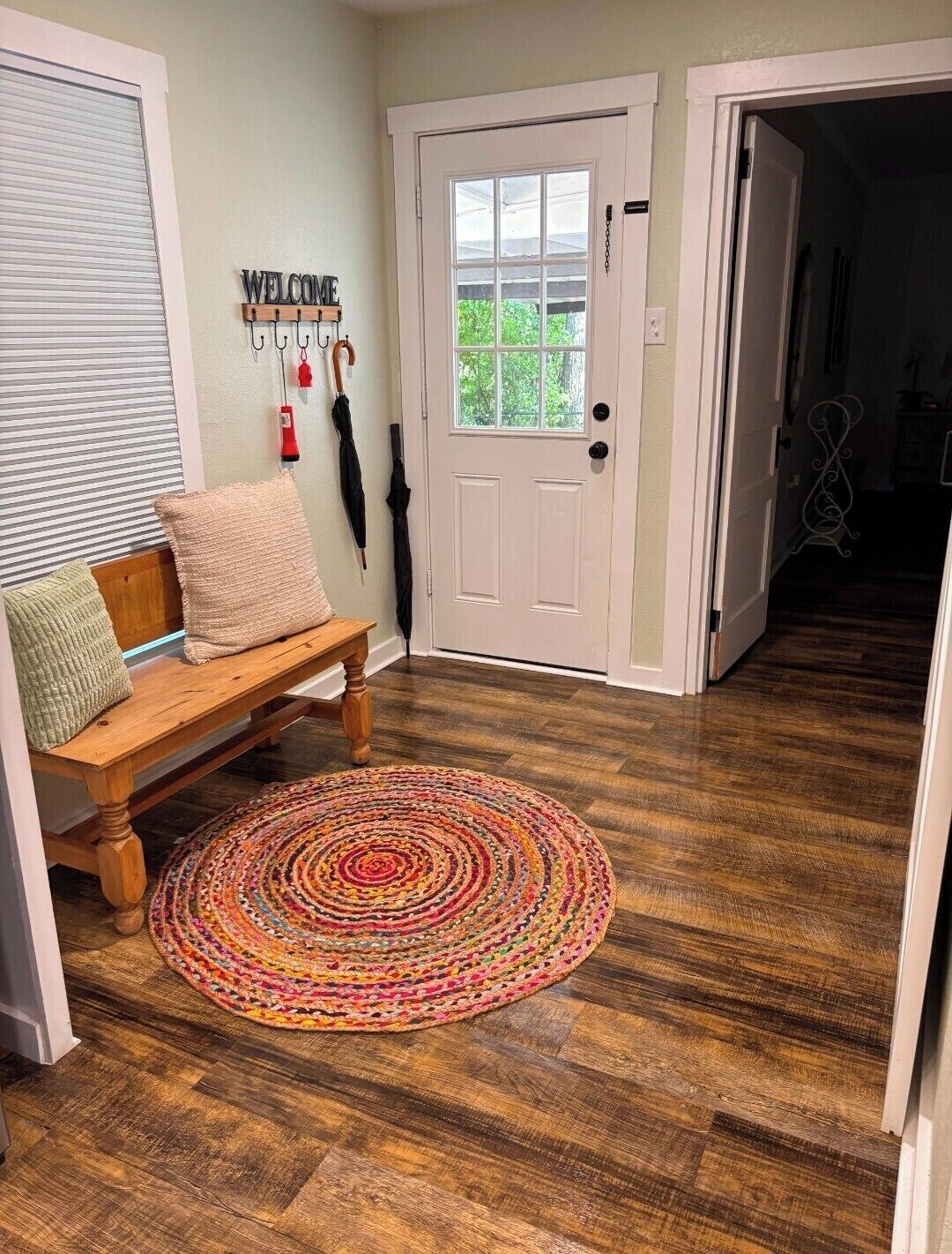 A wooden bench with cushions, a colorful woven rug, a white door with a window, and a 'WELCOME' sign.