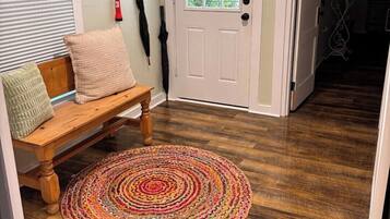 A wooden bench with cushions, a colorful woven rug, a white door with a window, and a 'WELCOME' sign.