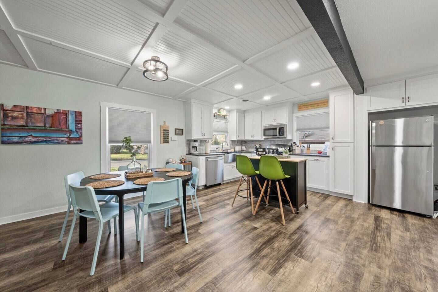 A modern kitchen with white cabinets, a stainless steel refrigerator, and a dining area with light blue chairs.