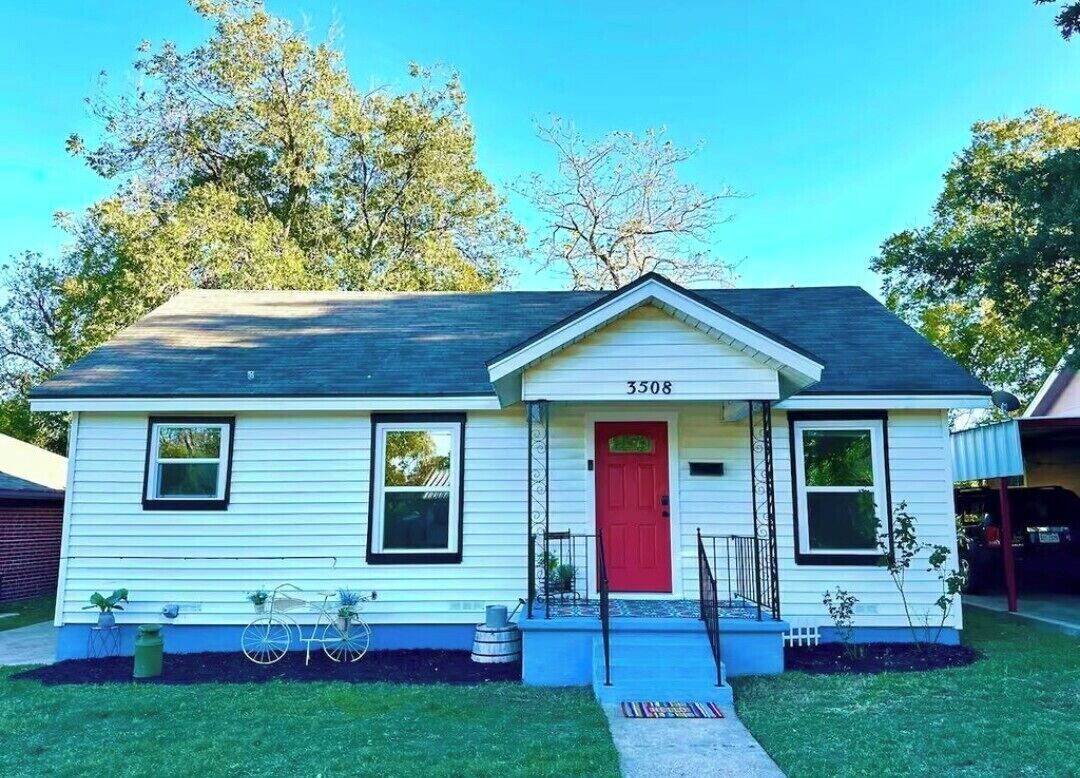 A single-story house with a red door, numbered 3508, featuring a front porch with a small step and a single window on each side.