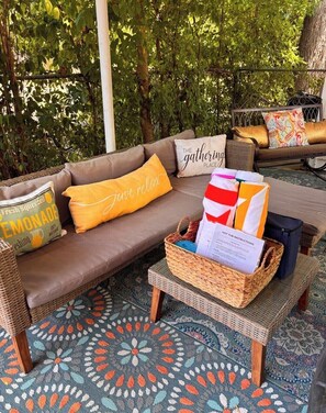 A wicker sofa with cushions, a woven basket with a hot tub instruction manual, and a patterned rug.
