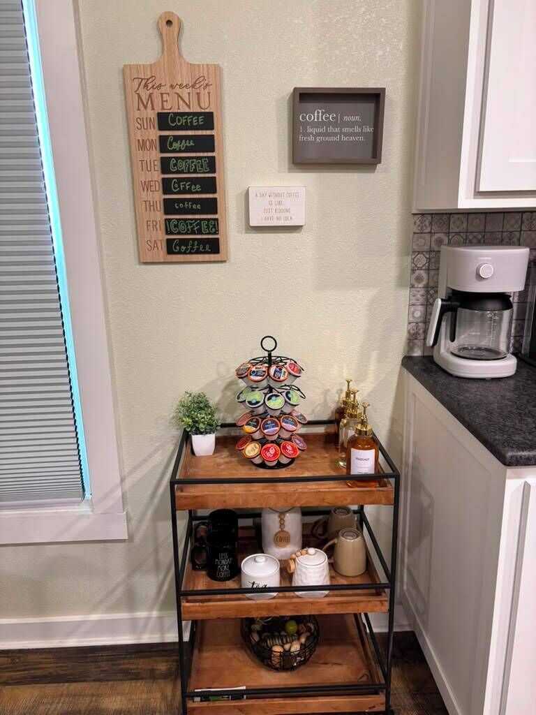 Uma cozinha com um cardápio de café na parede, uma máquina de café e uma estante com canecas e uma planta.