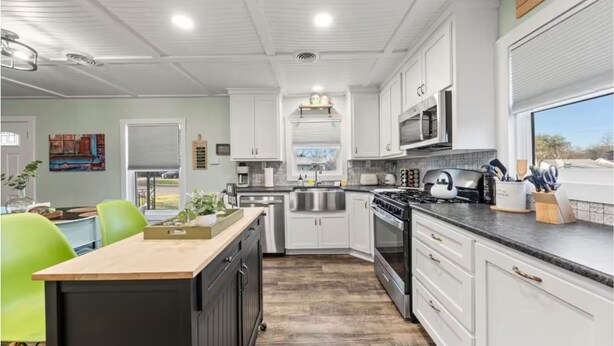 Une cuisine moderne avec des meubles blancs, une cuisinière, un four à micro-ondes et un coin repas agrémenté d’une chaise verte.