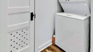 Une buanderie équipée d’un lave-linge et d’un sèche-linge, avec une porte blanche et un tapis à motifs sur le sol.
